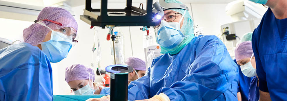 Chirurgen en medisch personeel voeren radiotherapie voor darmen uit in OK, met apparatuur en monitors op de achtergrond.