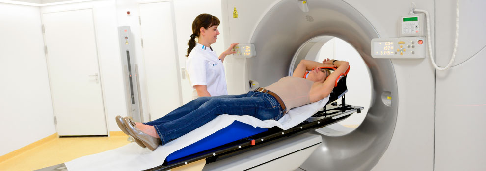 Een zorgverlener bereidt een patiënt voor op borstradiotherapie in een CT-scanner; de kamer is helder verlicht.