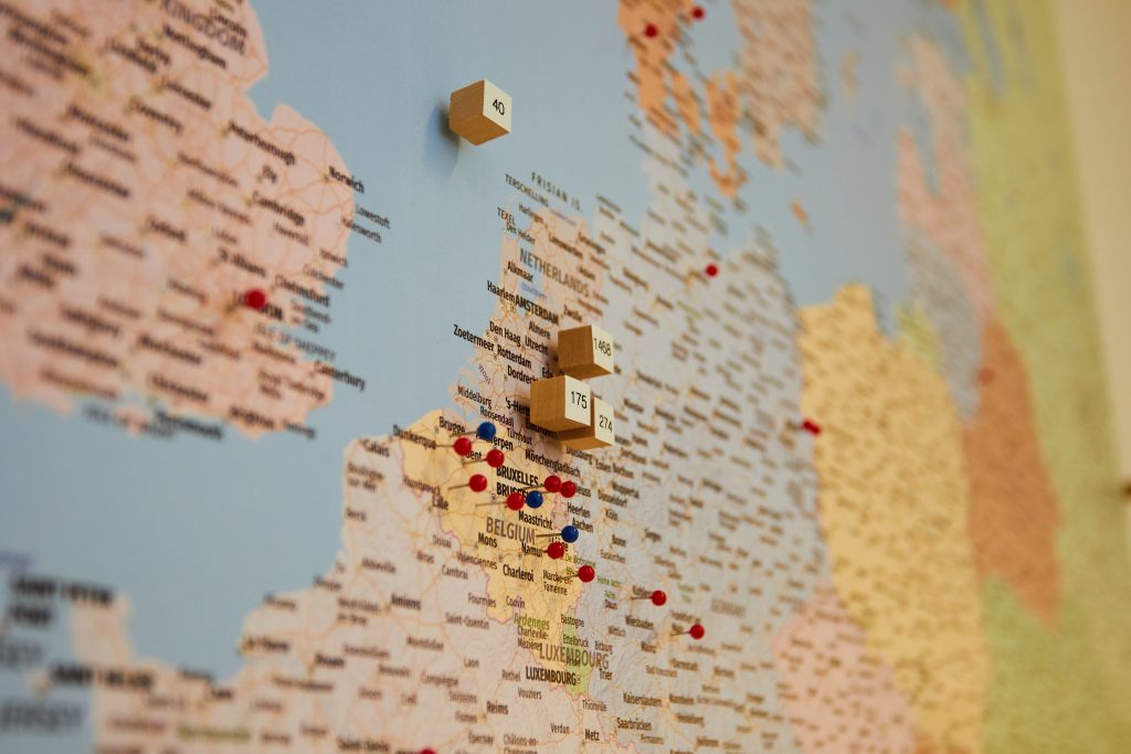 Kaart van West-Europa met rode en blauwe pinnen voor TOS-locaties; houten blokjes bij België, Nederland en Noord-Frankrijk.