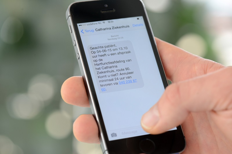 Hand met smartphone toont sms in het Nederlands over een ziekenhuisafspraak, duim raakt het scherm.