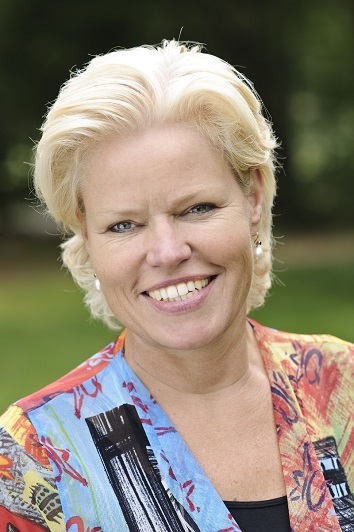 Geranne Engwirda van de Raad van Bestuur Catharina Ziekenhuis glimlacht, kort blond haar, gekleurde top, groene achtergrond.