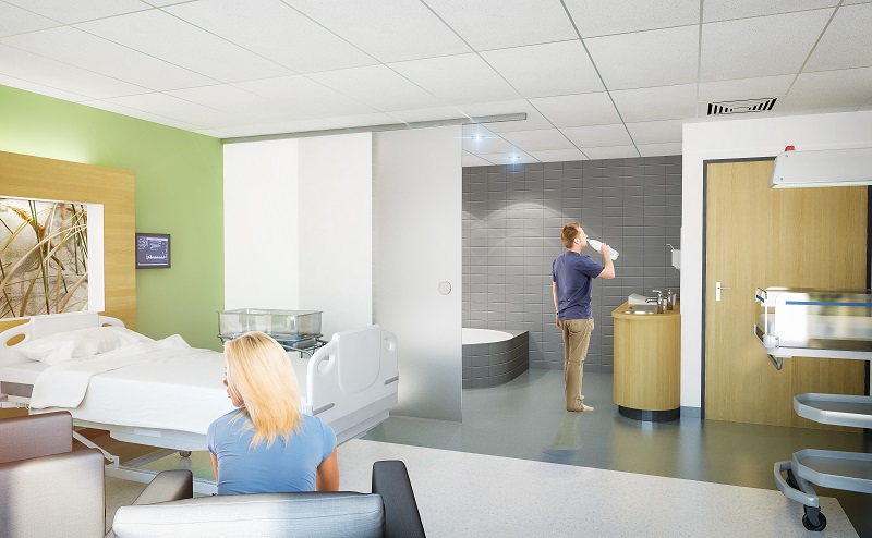 Moderne kraamsuite in Catharina Ziekenhuis met bed, vrouw op stoel, man bij wastafel en medische apparatuur. Groene muur.
