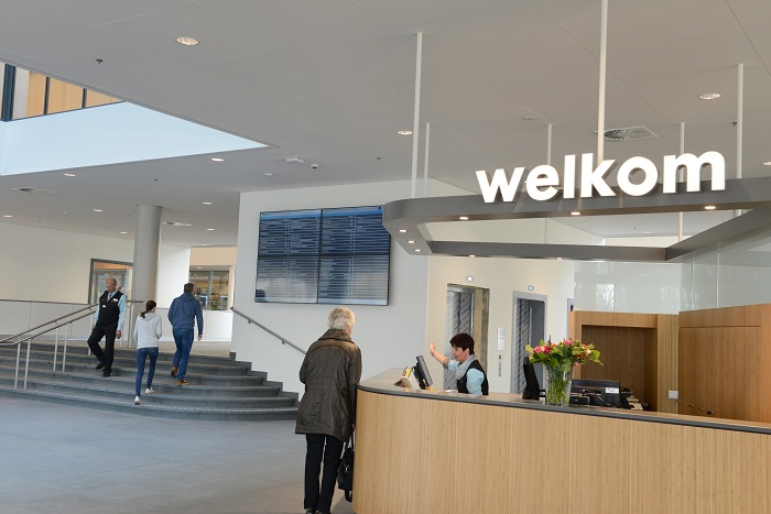 Moderne ontvangsthal Catharina Ziekenhuis met balie, medewerker helpt bezoeker, groot welkomstbord, mensen bij de hoofdingang.