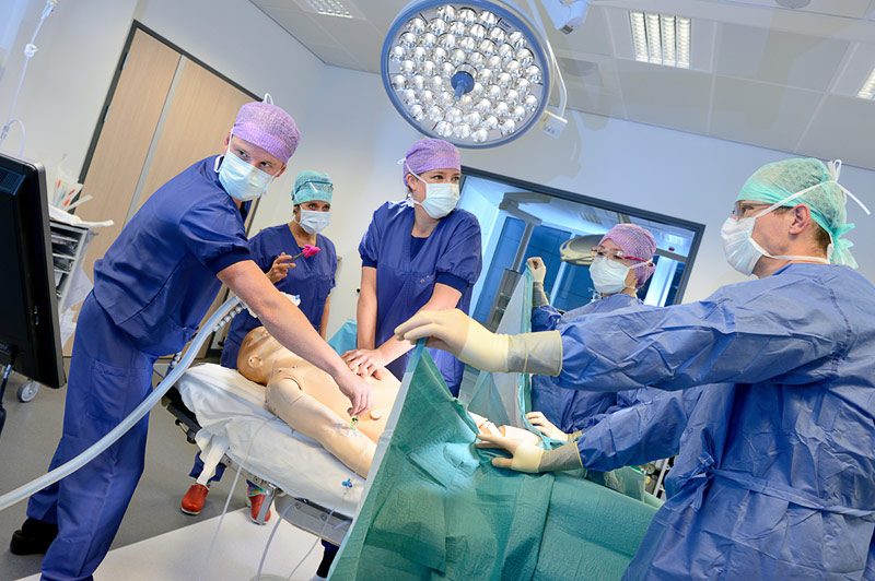 Vijf medisch specialisten in operatiekleding werken aan een oefenpop in een helder simulatiecentrum in het Catharina Ziekenhuis.