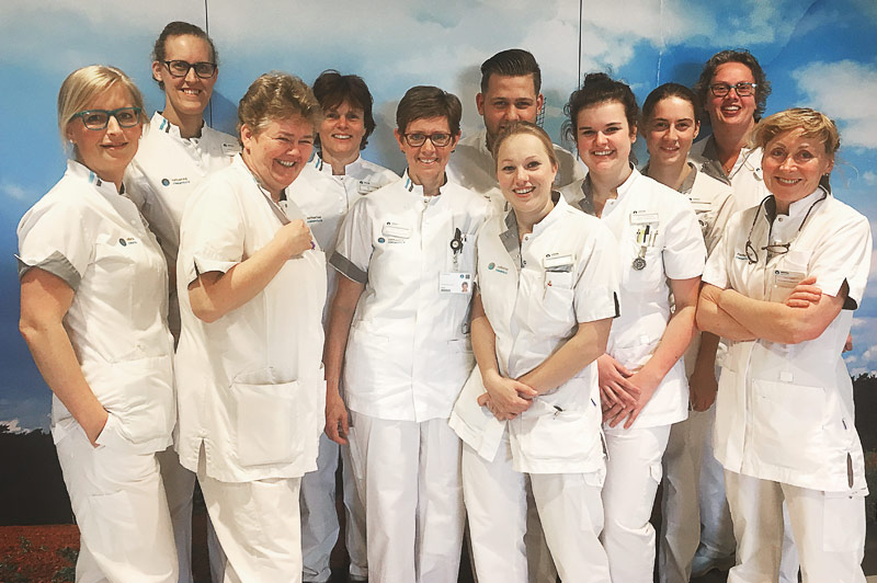 Elf verpleegkundigen in witte uniformen poseren binnen voor een lucht- en wolkenachtergrond op de Dag van de Verpleging.