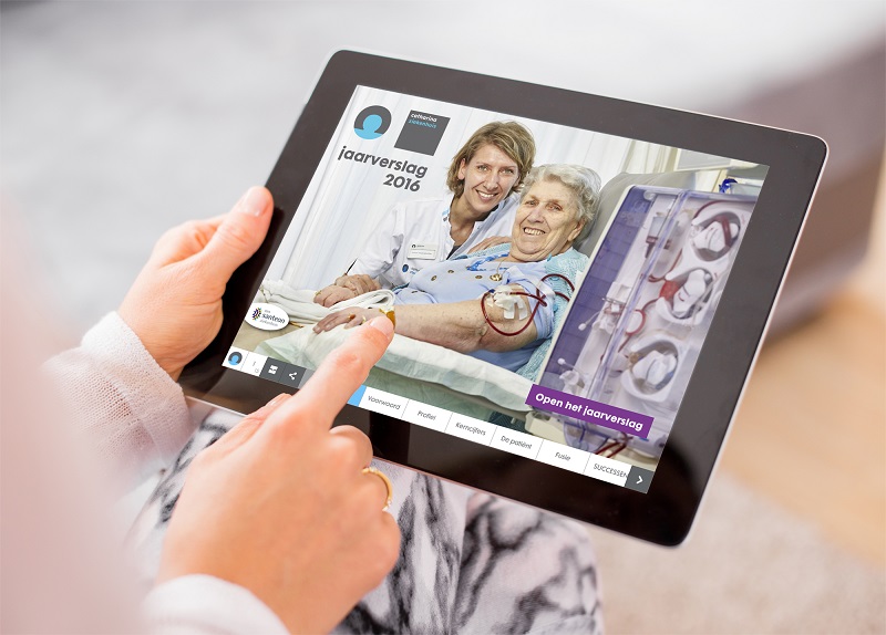 Persoon houdt tablet met cover van tijdschrift: patiënt in ziekenhuisbed, zorgverlener erbij; tekst over jaarverslag 2016 Catharina Ziekenhuis en focus op patiëntenzorg.