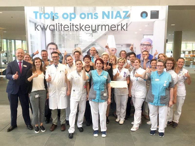 Zorgmedewerkers van Catharina Ziekenhuis in uniform geven duim omhoog voor een spandoek met 'Trots op ons NIAZ kwaliteitskeurmerk'.