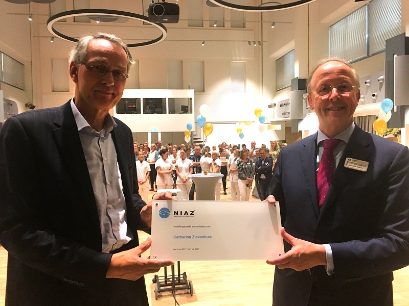 Twee mannen in pak houden binnen een certificaat vast met het Catharina Ziekenhuis. Op de achtergrond mensen en ballonnen.