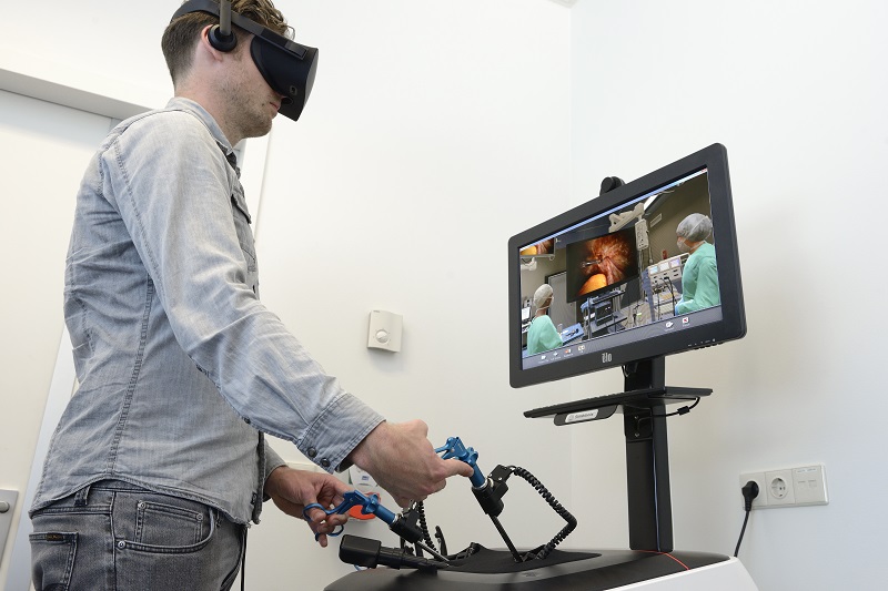 Iemand met een VR-bril gebruikt controllers bij een medische simulatie in het Catharina Ziekenhuis; monitor toont operatie.