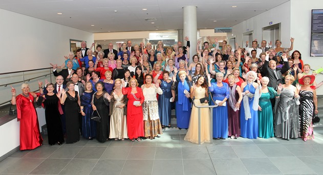 Een grote groep chique geklede oudere dames en heren poseert lachend en zwaaiend in een lichte zaal, hoogtepunten 2017.