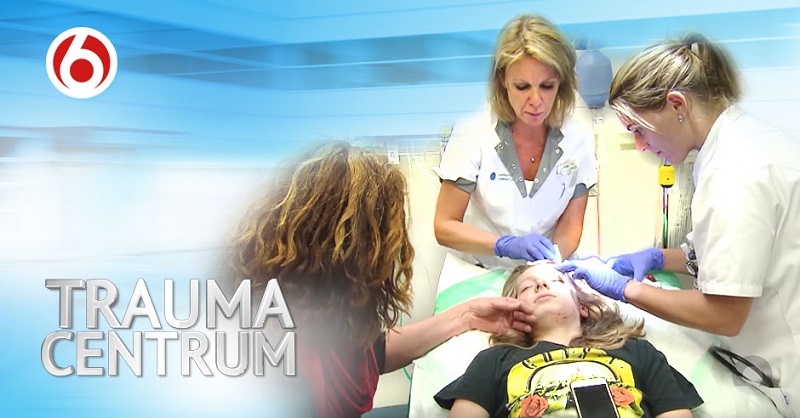 Twee artsen behandelen een jong patiëntje op een ziekenhuisbed, met "TRAUMA CENTRUM" en een rood logo op de voorgrond.