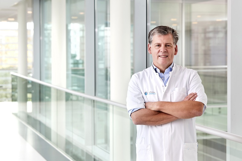 Man in witte doktersjas met gekruiste armen in lichte bende, klaar om apneu-patiënten te helpen met snurken en slaapgezondheid.