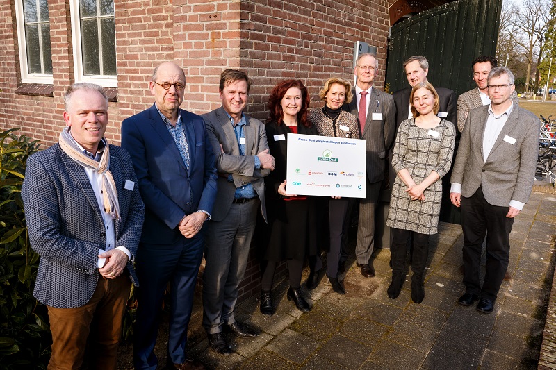 Tien mensen poseren buiten voor een bakstenen gebouw met een Greendeal-bord bij het Catharina Ziekenhuis.