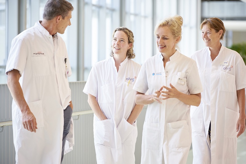 Vier zorgprofessionals in witte jassen lopen pratend door een lichte bende in het Catharina Ziekenhuis. Drie vrouwen, één man.