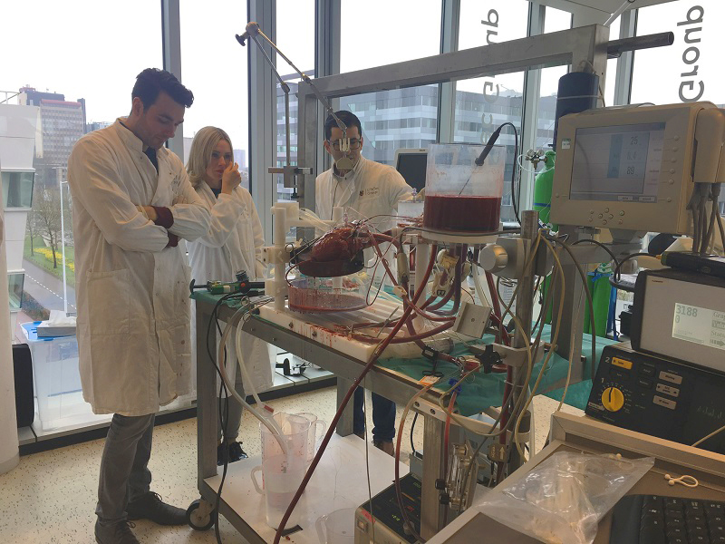 Drie mensen in labjassen werken aan een medisch apparaat met slangen en rode vloeistof in een Eindhovense laboratoriumruimte.