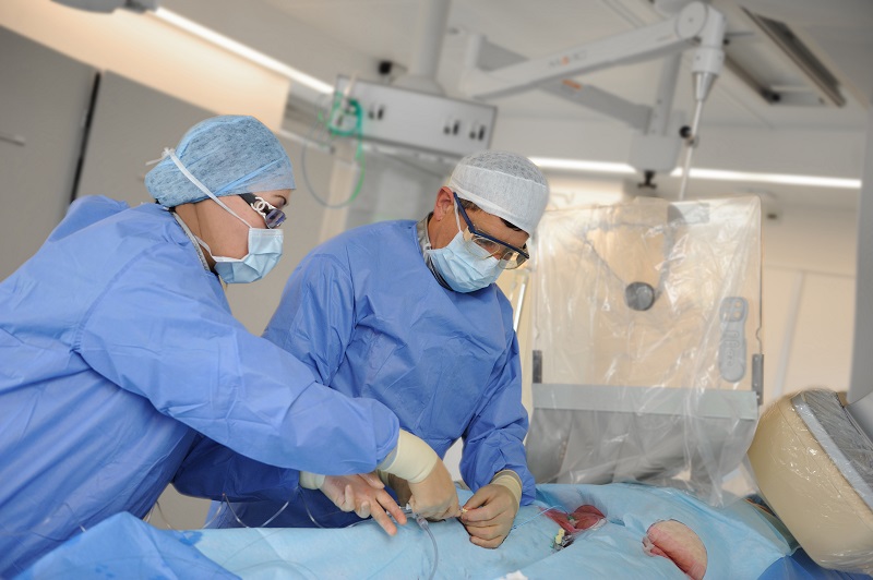 Twee medici in OK-kleding voeren een bypassoperatie uit in een operatiekamer met moderne apparatuur en lampen.