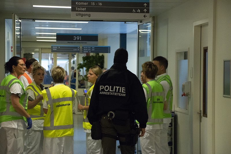 Ziekenhuismedewerkers in gele hesjes praten met een politieagent in Arrestatieteam-vest na een geslaagde crisisoefening.
