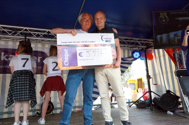 Twee mannen op een podium met cheque voor Catharina Ziekenhuis bij SamenLoop voor Hoop; 2 mensen onder blauw-witte tent.