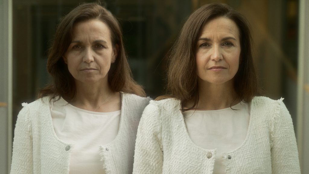 Twee vrouwen met lang bruin haar en vergelijkbare trekken staan binnen naast elkaar en kijken samen in de camera.