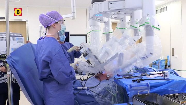 Twee chirurgen bedienen een robotsysteem tijdens een kankerbehandeling; één aan de console, één bij de patiënt. Apparatuur op voorgrond.