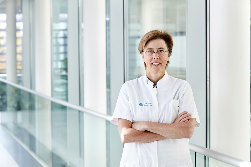 Persoon met bril en witte zorgkleding staat met gekruiste armen in lichte gang van Catharina Ziekenhuis, expert in HIPEC.
