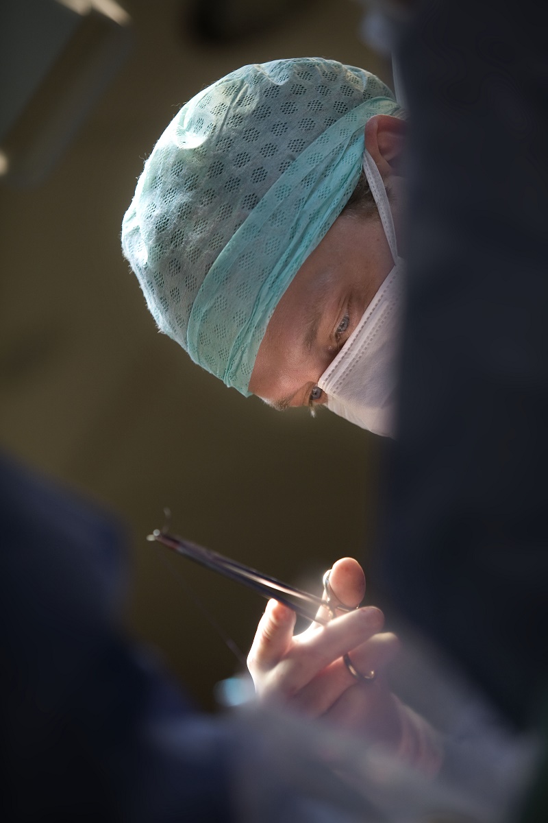 Een arts met een operatiemuts en -masker voert een operatie uit bij een patiënt met darmkanker.