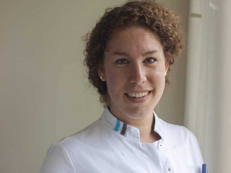 Vrouw met krullend bruin haar in wit-blauw medisch uniform lacht binnen en specialiseert zich in baarmoedergolven voor vruchtbaarheid.