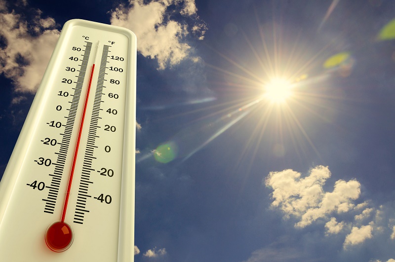 Thermometer met hoge temperaturen voor een felle zon en deels bewolkte lucht, wijzend op tropisch warm weer.