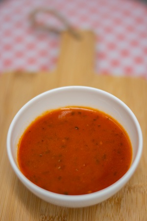 Klein wit schaaltje met rode tomatensaus op houten oppervlak, wazige achtergrond met roze-wit ruitpatroon, aanbevolen bij chemotherapie.
