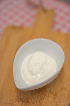 Een klein wit schaaltje met een portie romige yoghurt op een houten ondergrond, aanbevolen tijdens chemotherapie.