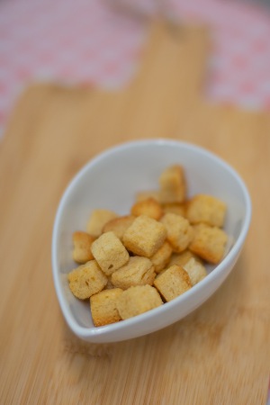 Witte kom met goudbruine croutons op houten ondergrond, vage roze achtergrond. Aanbevolen door diëtisten bij chemotherapie.