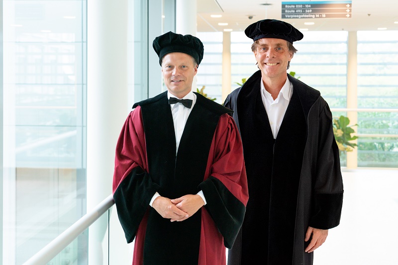 Twee mannen in toga's en baretten, mogelijk van het Catharina Ziekenhuis, staan in een lichte, moderne bende.