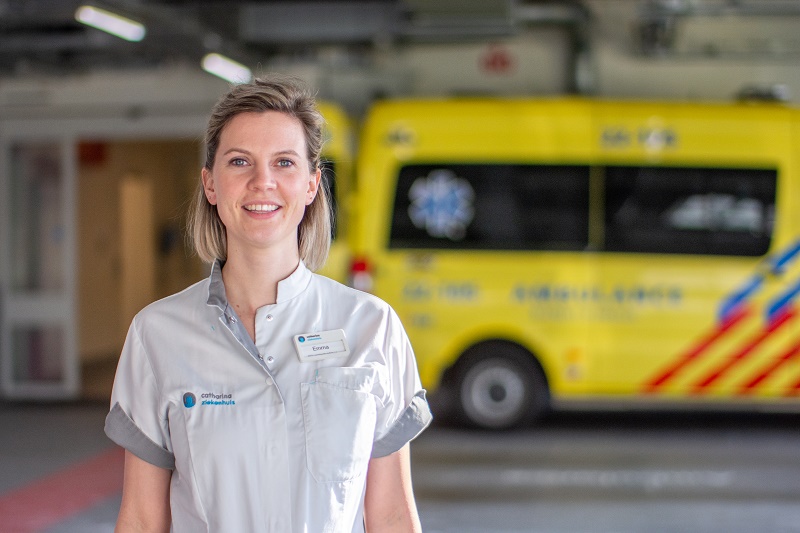 Een vrouw in medisch uniform staat glimlachend voor een gele ambulance bij het Catharina Ziekenhuis.