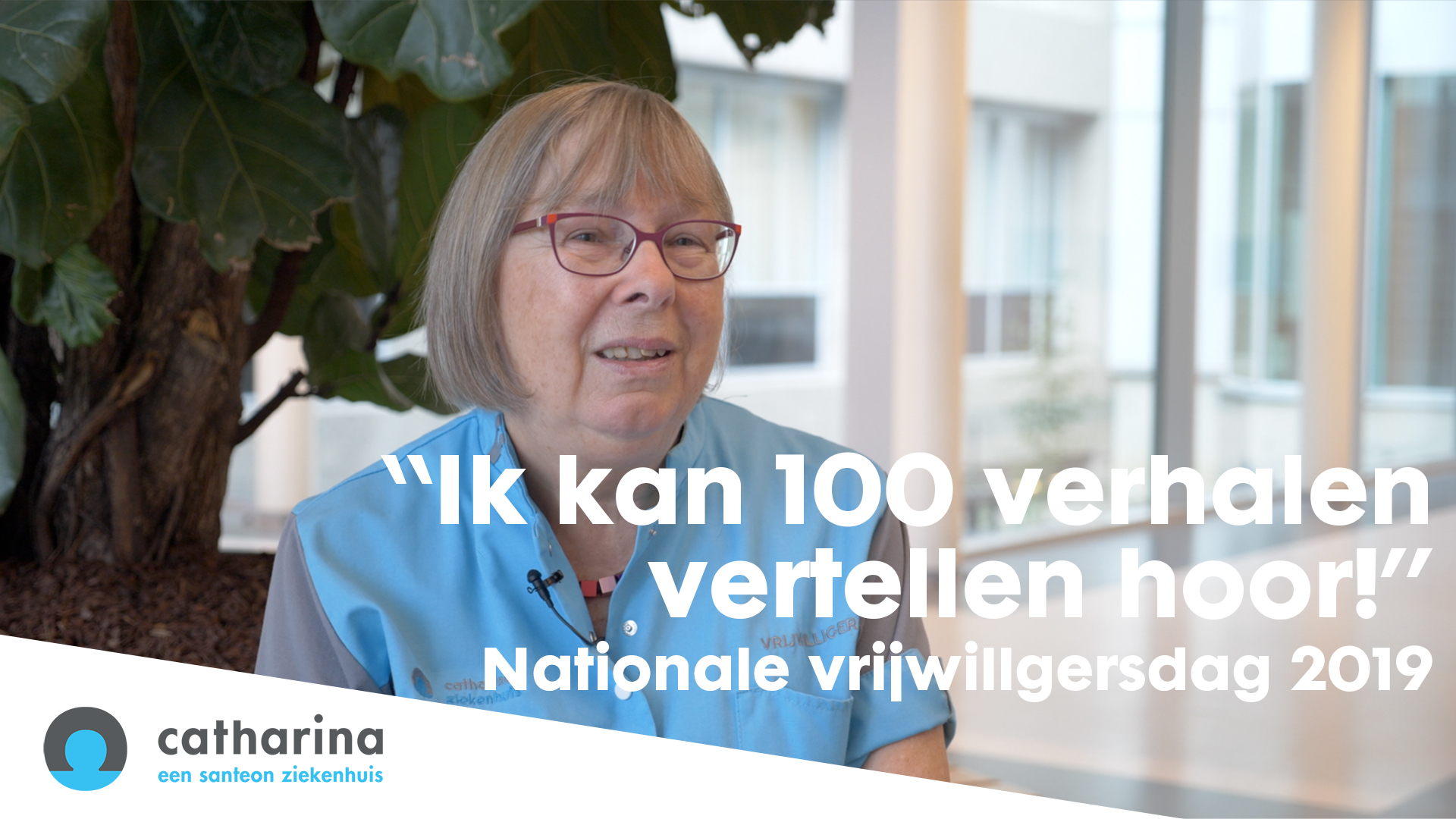 Oudere vrouw met blauw vest, bril en naamkaartje zit binnen naast grote plant. Tekst: Ik kan 100 verhalen vertellen hoor.