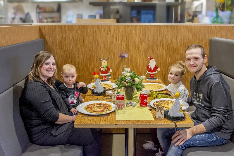 Een gezin van vier aan een restauranttafel, lachend. Op tafel staan pannenkoeken en kerstversiering.