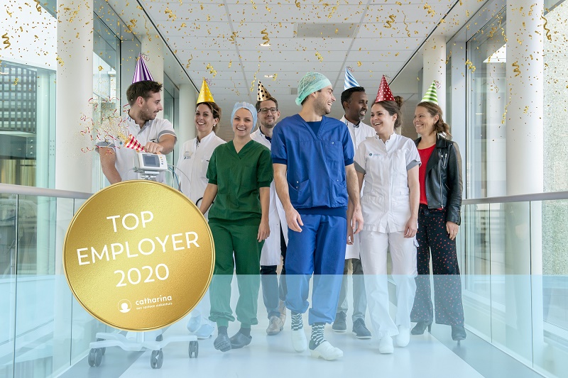Zorgmedewerkers van Catharina Ziekenhuis, met feesthoedjes, lopen lachend door de bende. Confetti en Top Employer 2020-badge zichtbaar.