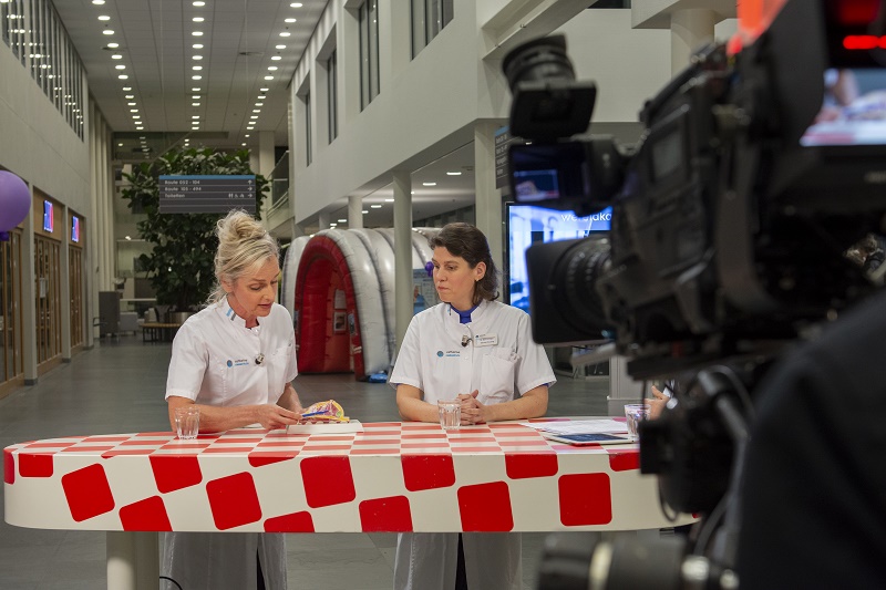 Twee mensen in witte uniformen zitten aan een rood-wit geblokte tafel binnen en bespreken iets, met glazen water op tafel.