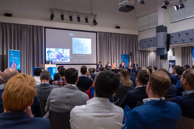 Een volle zaal kijkt naar zes panelleden, waaronder Eindhovense cardiologen. Op het scherm een video-oproep en medisch beeld.