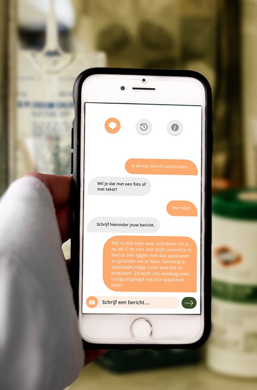 Een hand houdt een smartphone vast met een Nederlandse chat op een wit-oranje app; de achtergrond is vaag en onscherp.