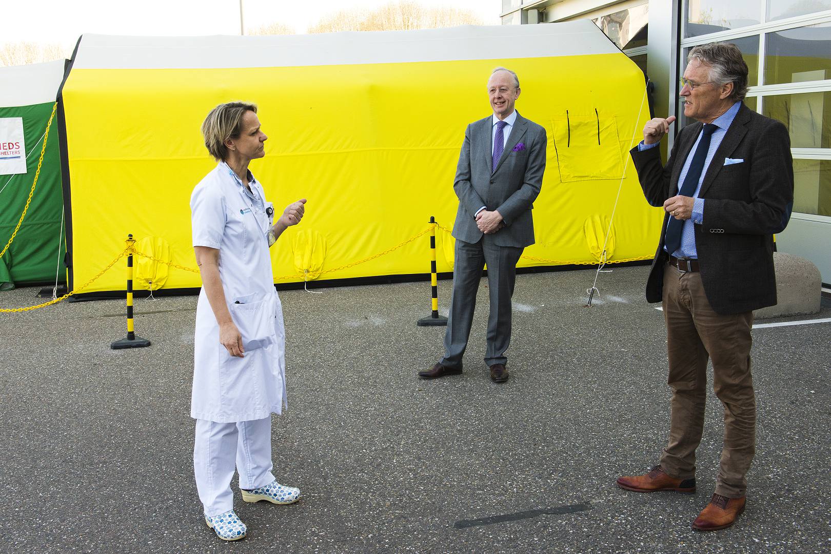 Drie volwassenen bij een geel-groene tent voor het Catharina Ziekenhuis, in gesprek over corona-afdelingen.