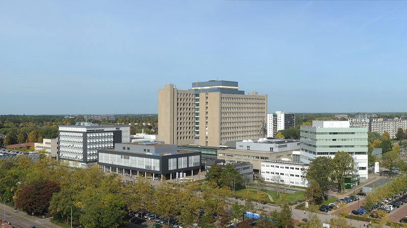 Een groot ziekenhuiscomplex met meerdere moderne gebouwen, omgeven door bomen, parkeerplaatsen en wegen op een heldere dag.