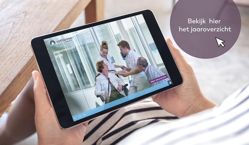 Persoon houdt tablet met jaaroverzicht 2019 Catharina Ziekenhuis; afbeelding van verpleegkundige en patiënt in rolstoel.