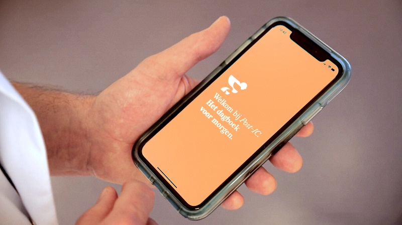 Persoon houdt smartphone met oranje scherm vast waarop witte Nederlandse tekst staat: "Welkom bij Post-IC dagboek".