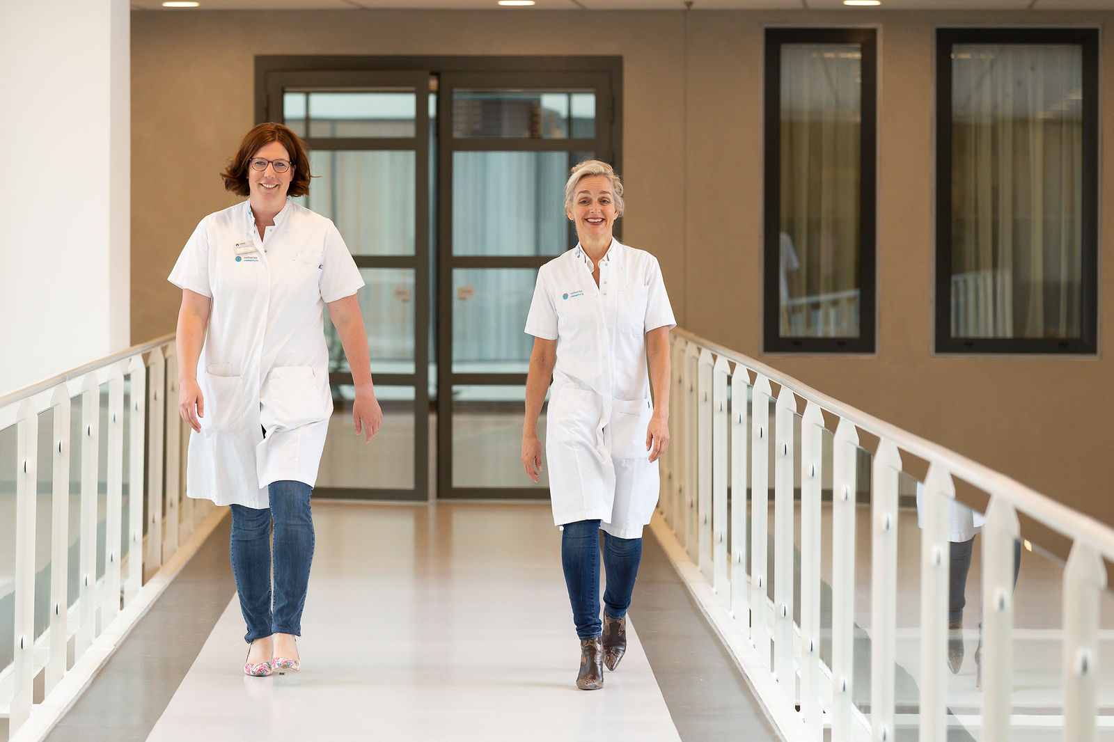 Twee vrouwen in witte jassen lopen door een lichte ziekenhuishal en bespreken de nieuwste resultaten van borstkankeronderzoek.