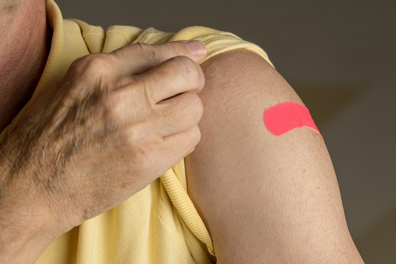 Persoon in geel shirt toont roze pleister op bovenarm, mogelijk na BCG-vaccinatie in Catharina Ziekenhuis.