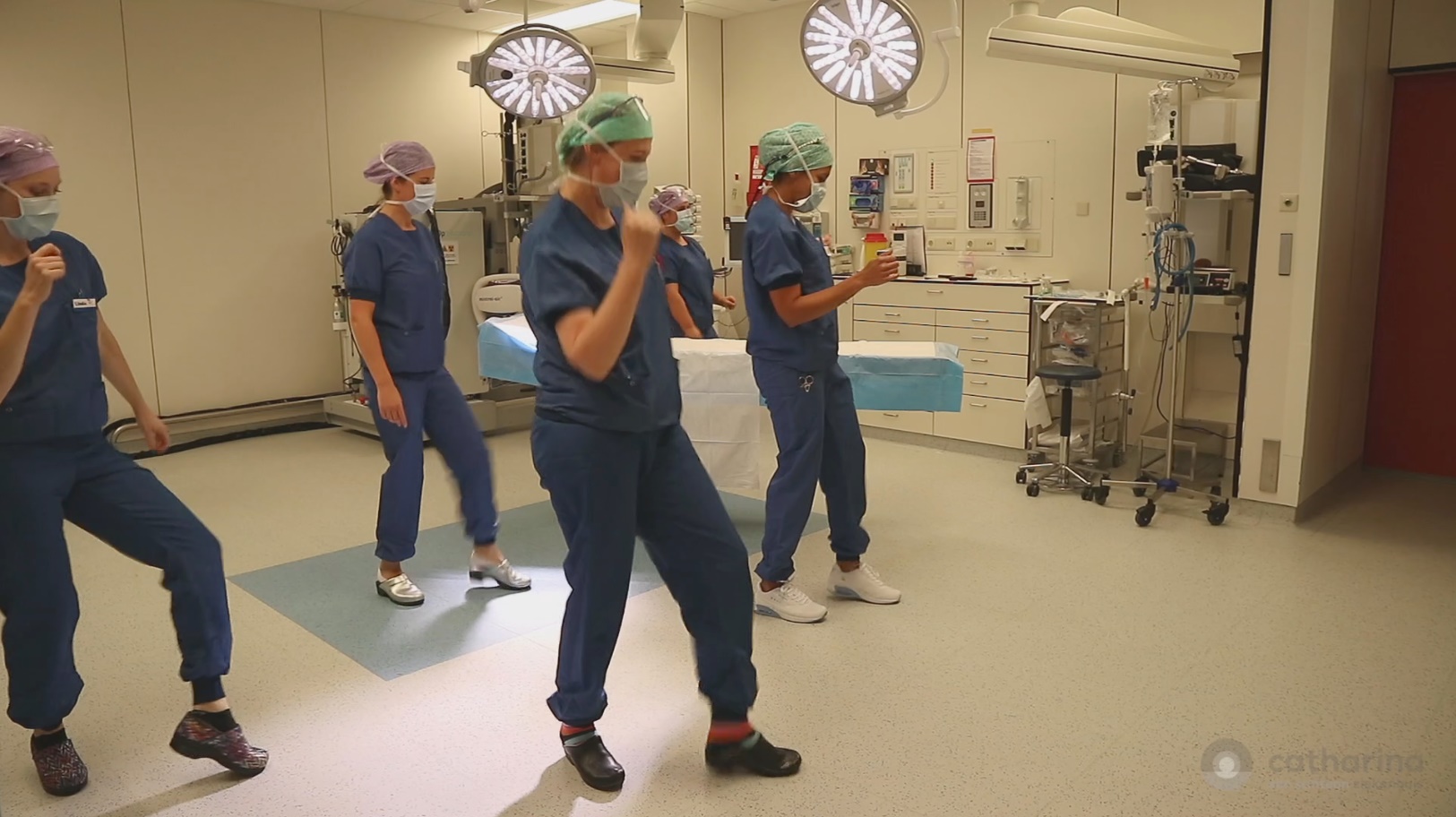 Vier Catharina-medewerkers in OK-kleding dansen de Jerusalema Challenge in een operatiekamer tussen medische apparatuur.