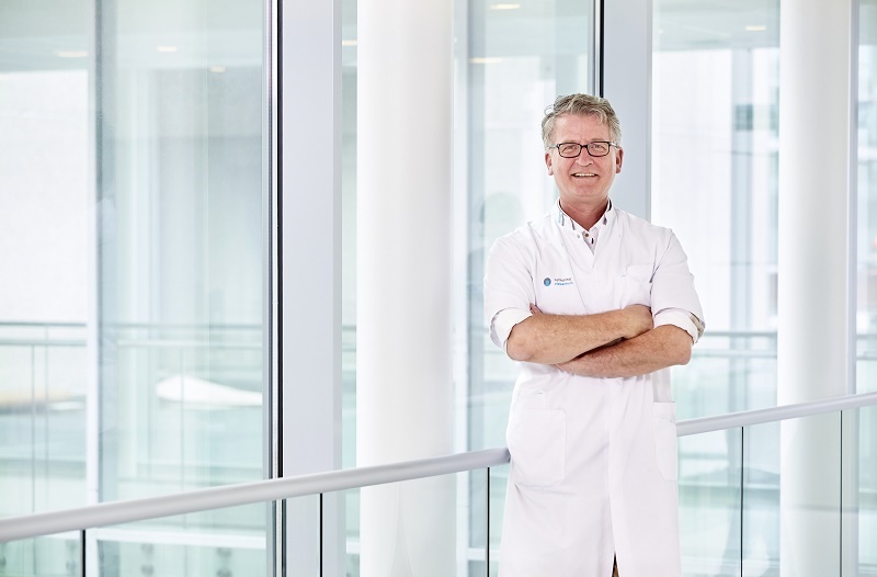Man in witte jas met gekruiste armen in modern gebouw van Catharina Ziekenhuis, expert in endometriosebehandeling.