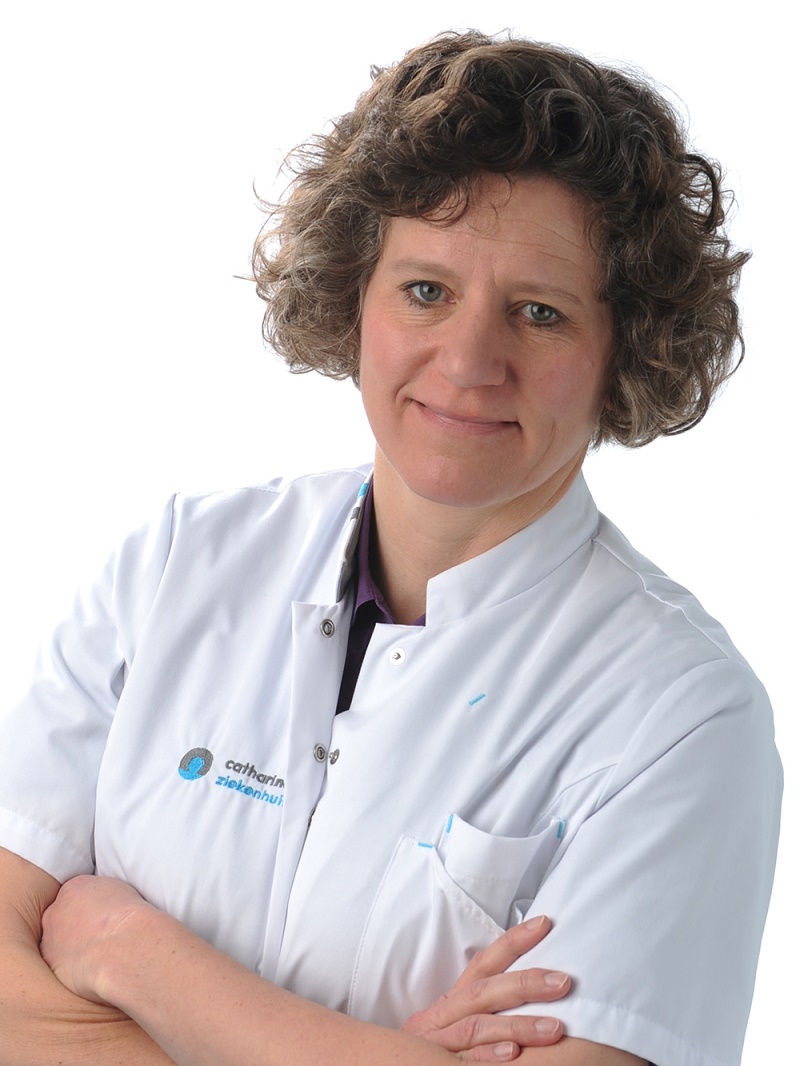 Geriater Judith Wilmer met kort, krullend haar in witte jas van Catharina Ziekenhuis, armen over elkaar, op witte achtergrond.