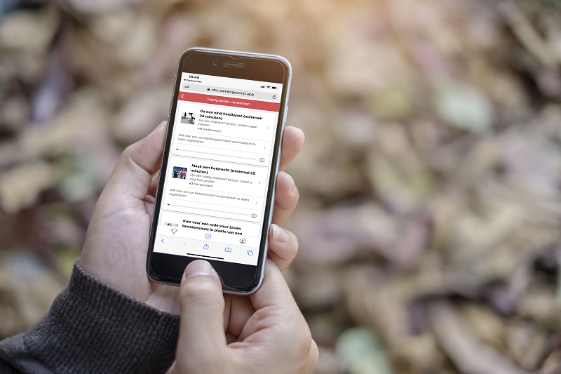 Iemand houdt een smartphone vast met nieuws over leefstijlprogramma's tegen hart- en vaatziekten, op de achtergrond droge bladeren.