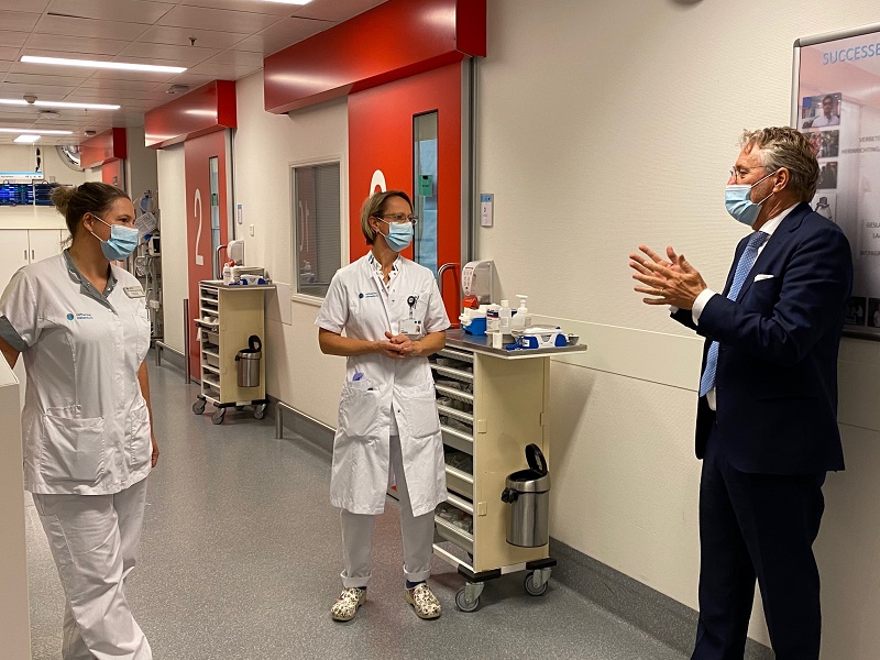 Burgemeester Jorritsma gebaart in Catharina Ziekenhuis; twee medewerkers in witte uniformen luisteren, allen dragen mondkapjes.